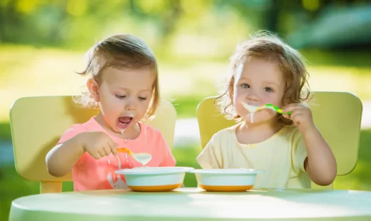 two-little-2-years-old-girls-sitting-table-eating-together-against-green-lawn_155003-13550